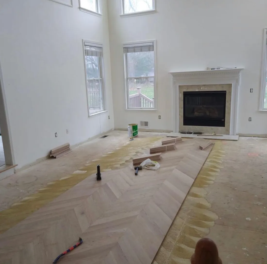 Herringbone planks being laid across a living room subfloor