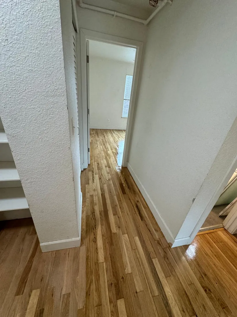 Freshly refinished hallway floor running toward a bright doorway